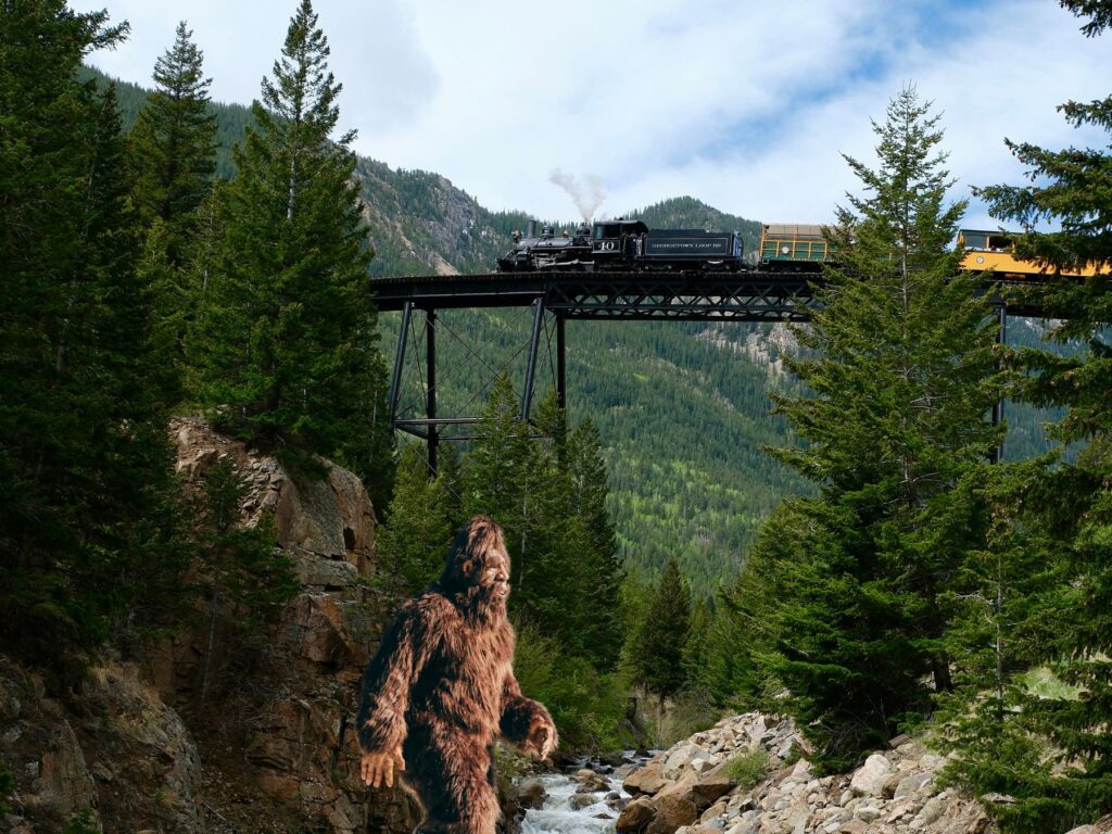 Train crossing bridge with Sasquatch walking across forest