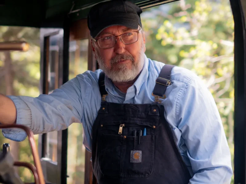 Friendly Georgetown Loop Railroad locomotive engineer in overalls working in steam engine cab