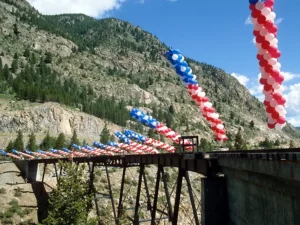 Red, white, and blue balloon arches decorating the Georgetown Loop Railroad high bridge with Rocky