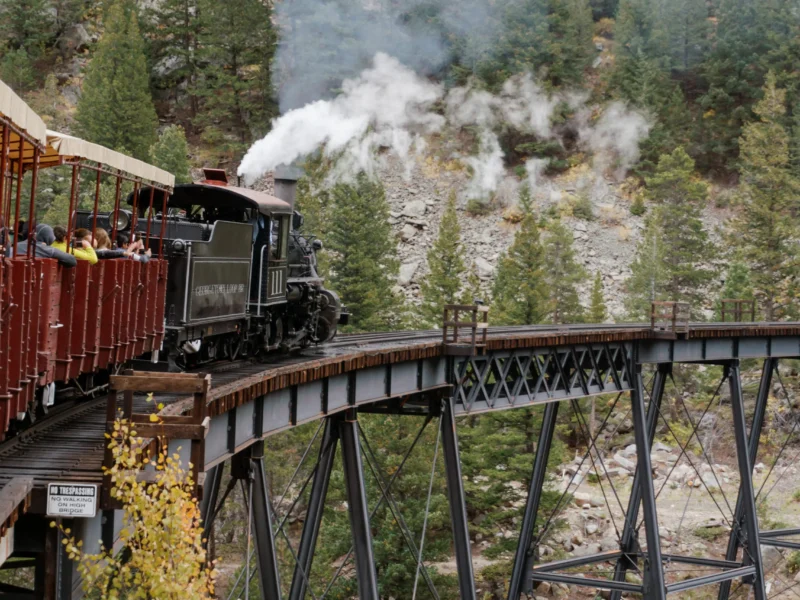 Steam locomotive pulling open-air passenger cars across the Georgetown Loop high bridge surrounded