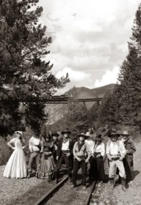 Sepia-toned group photo of the full Wild West Days cast in period costumes gathered on the railroad