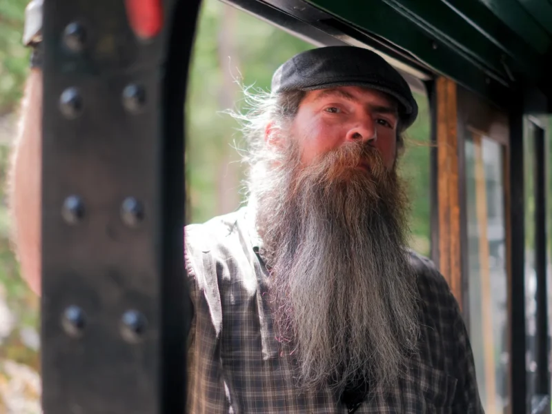 Bearded Georgetown Loop Railroad locomotive engineer in train cab wearing vintage-style cap