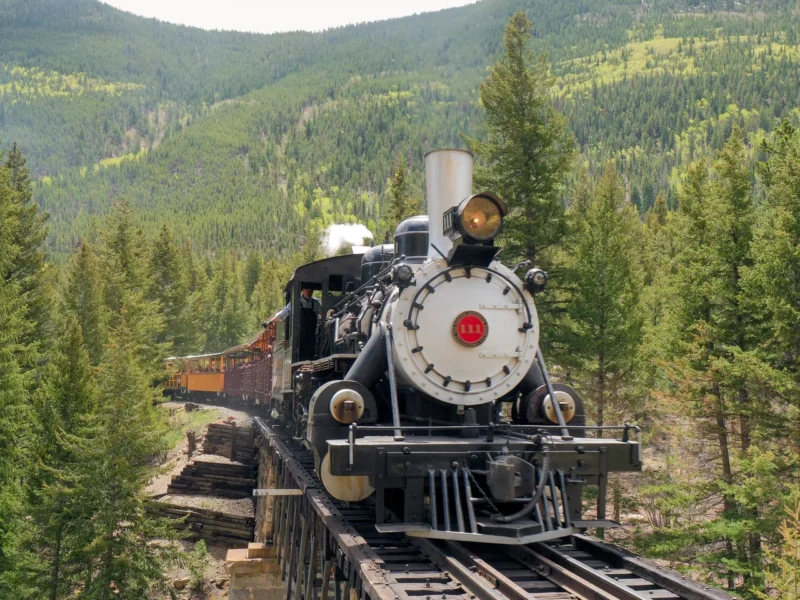 Historic steam locomotive approaching through Georgetown Loop mountain valley surrounded by