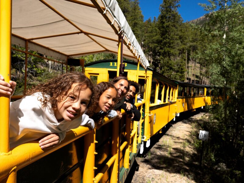 People leaning over side of train car with bridge in background