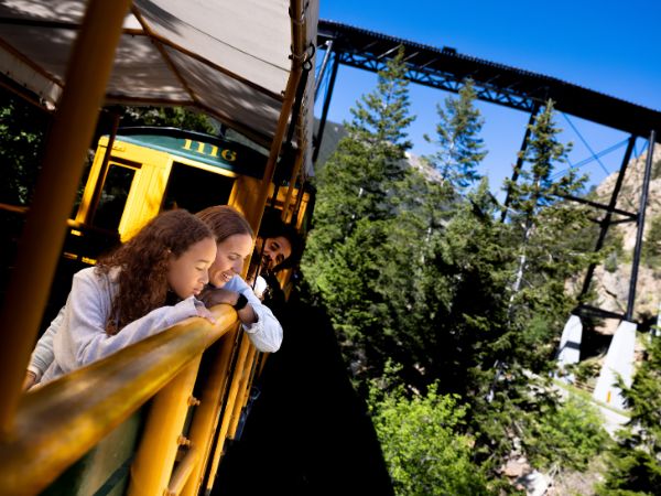 People leaning over side of train car with bridge in background